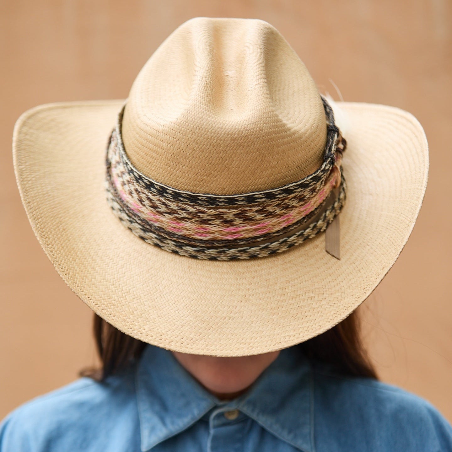 Close-up styling of multiple hand-braided horsehair hatbands, featuring cream, black, and pink chevron weaves on a sand-colored western straw hat.